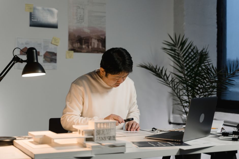 Architect reviewing building models and designs at a work desk under soft lighting in a modern office setting.